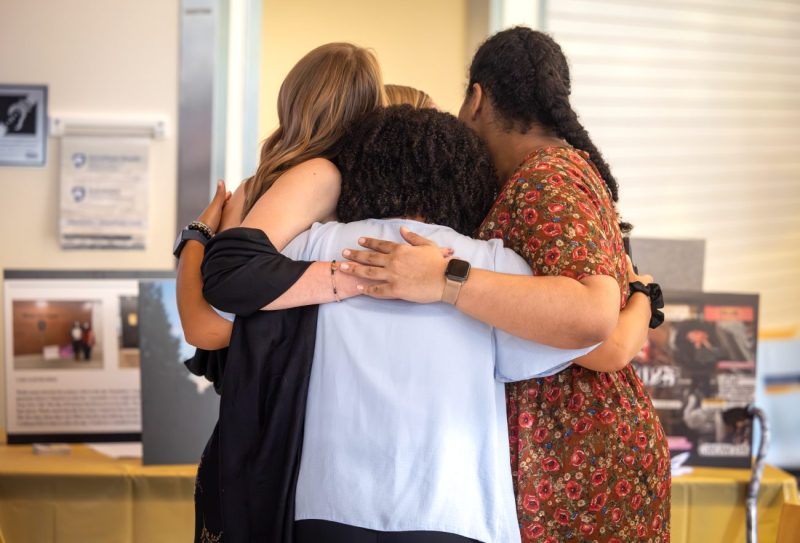 Four childhood cancer survivors embrace during the Photovoice art exhibit on Tuesday, Sept. 30, 2025. The Penn State Health Children’s Hospital Childhood Cancer Survivorship Clinic hosted the art exhibit featuring the work of five childhood cancer survivors who participated in its inaugural the Photovoice program.