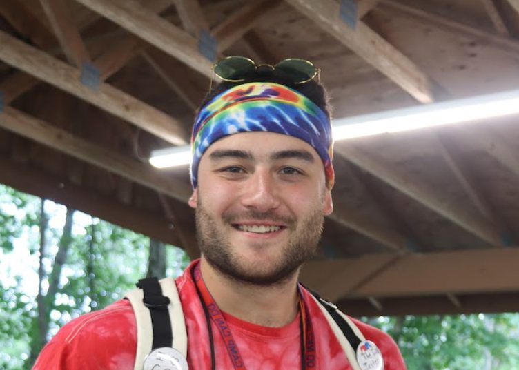 Nick smiles while wearing a colorful headband and backpack during an outdoor camp activity.