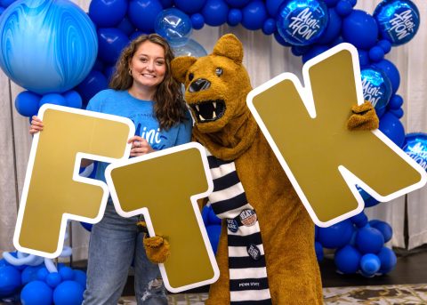 Lauryn poses with Penn State Nittany Lion mascot holding &ldquo;FTK&rdquo; letters at a Mini-THON event, surrounded by blue balloon decorations.