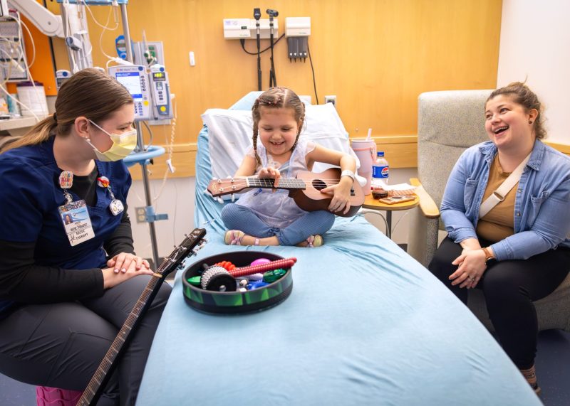 Bella smiles while playing a ukulele during music therapy at Penn State Health Golisano Children’s Hospital during her leukemia journey.