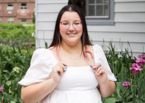 Angele poses outdoors with a stethoscope after graduating from nursing school.