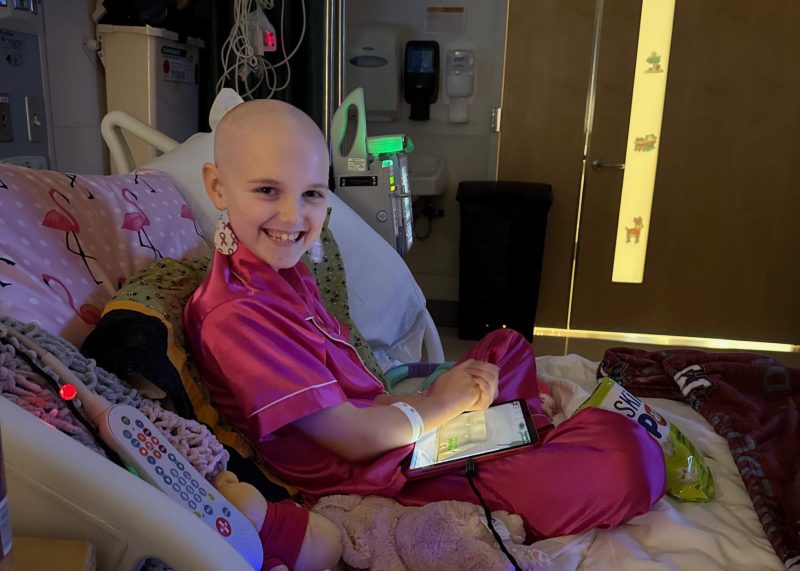 Lenny smiles while sitting in a hospital bed wearing bright pink pajamas during childhood cancer treatment.