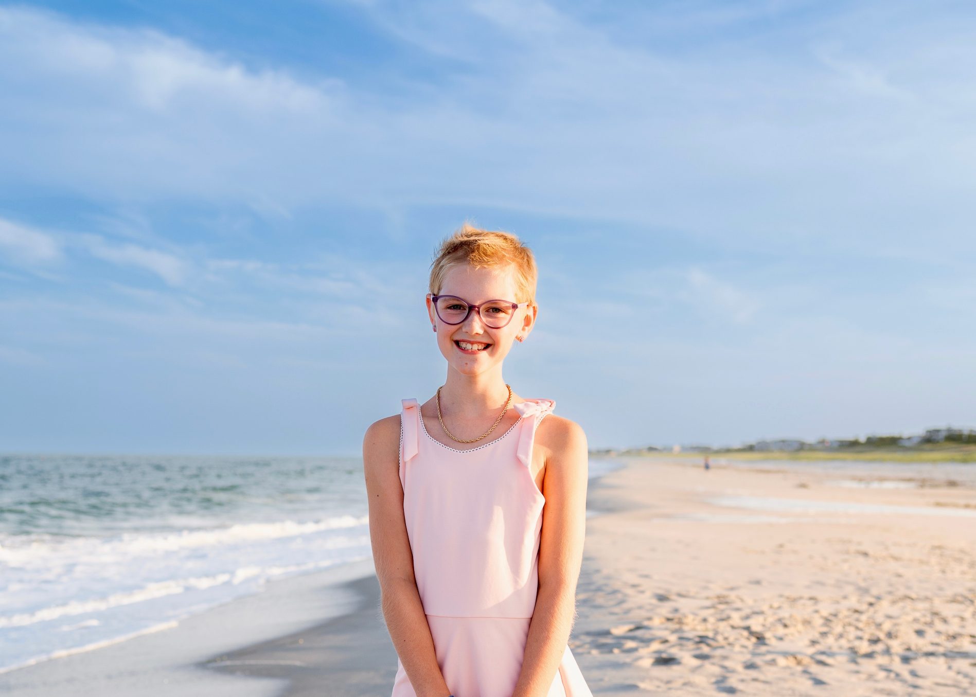Lenny smiles on the beach in a pink dress after completing childhood cancer treatment.
