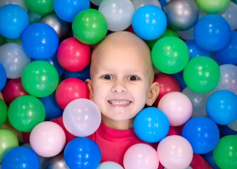 Four Diamonds child Presley, who is undergoing treatment for a Wilms tumor, smiles while surrounded by colorful balls in a ball pit.