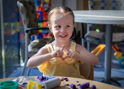 A smiling young pediatric cancer patient makes a diamond shape with her hands while playing at the Four Diamonds clinic.