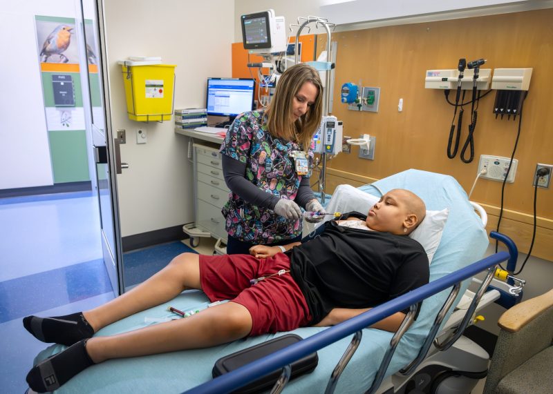 A nurse provides treatment to a pediatric cancer patient resting in a hospital bed at the Four Diamonds clinic.