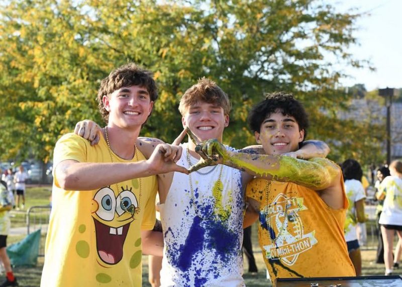 Three Cumberland Valley Mini-THON students covered in blue and gold paint make a diamond with their hands.
