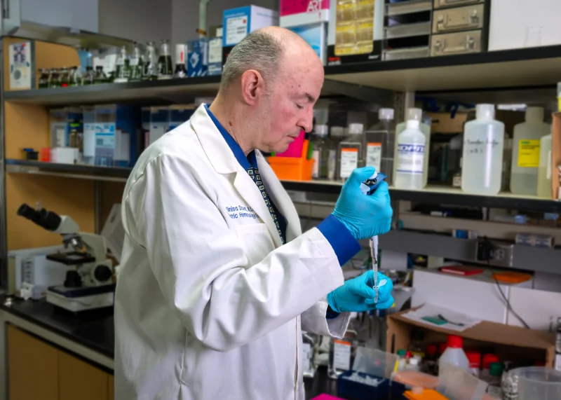 Researcher in a laboratory coat and blue gloves uses a pipette to conduct pediatric cancer research supported by Four Diamonds.