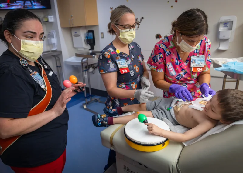 Three pediatric care providers engage a young child in a music activity during treatment, illustrating the comprehensive support provided to Four Diamonds families.